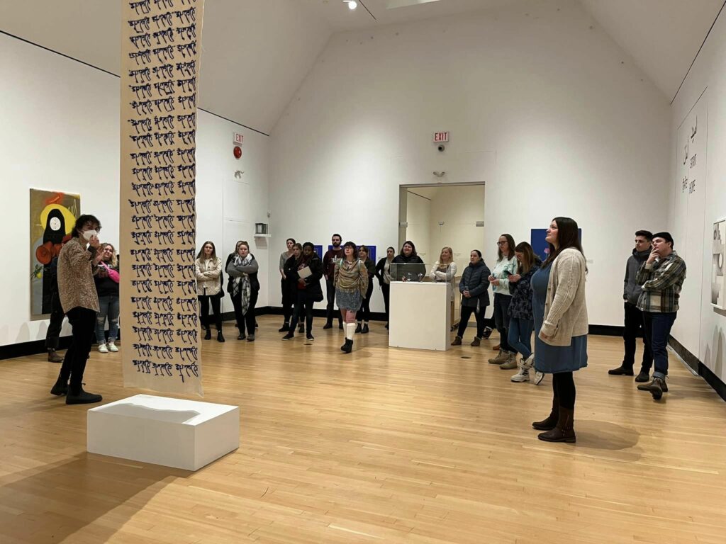 A group photo of the teacher candidates looking at on of the pieces in the gallery.