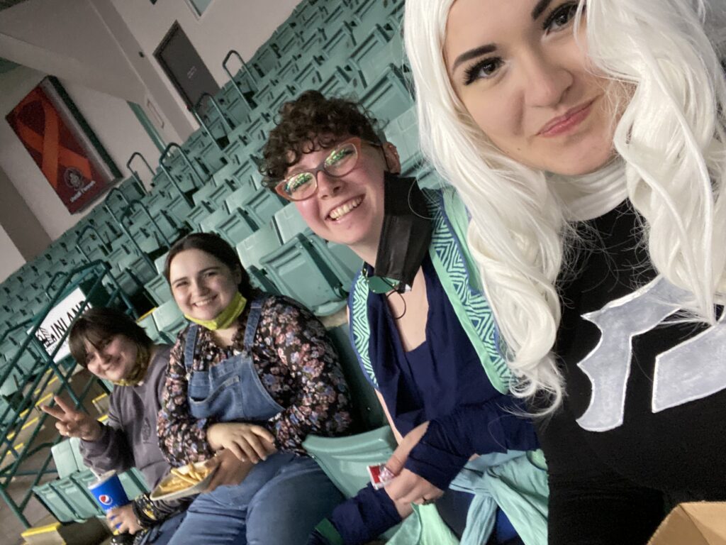 A picture of 4 people eating lunch at a convention. They are sat in a row in arena seating.